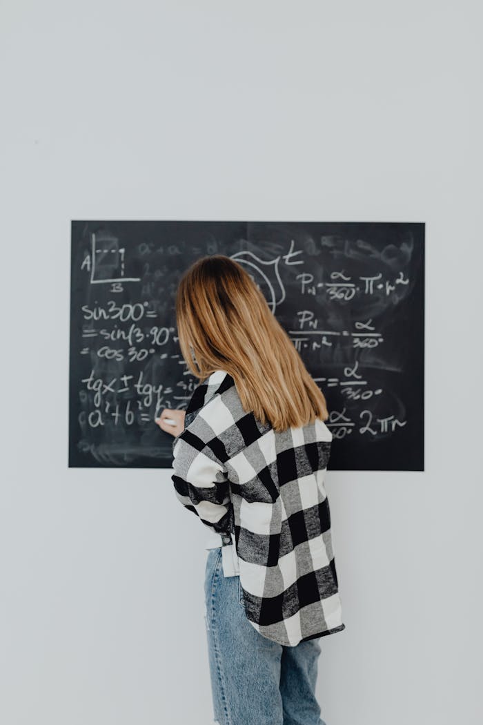Teenager writing mathematical formulas on a blackboard in a classroom setting.
